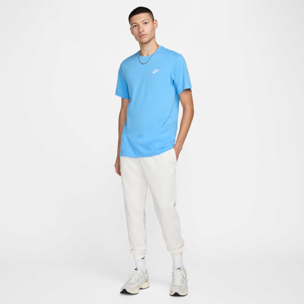 Person wearing a blue t-shirt with a logo and white pants on a white background